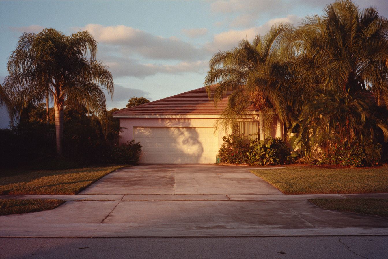 A South Florida house at dusk, palms over an empty driveway
